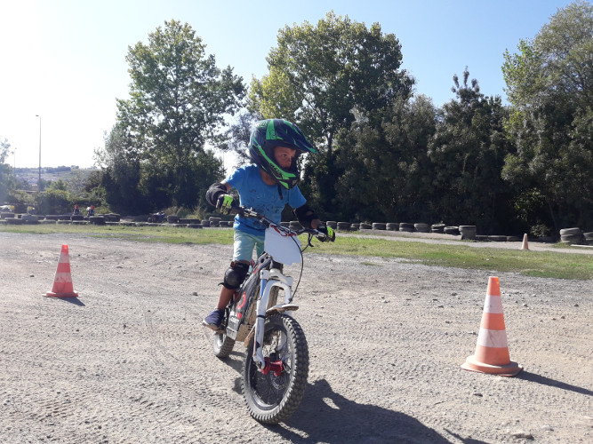 un enfant cherche l'équilibre debout sur sa moto de trial et effectue un slalom
