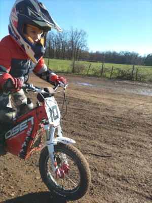 un enfant cherche l'équilibre debout sur sa moto de trial et effectue un slalom
